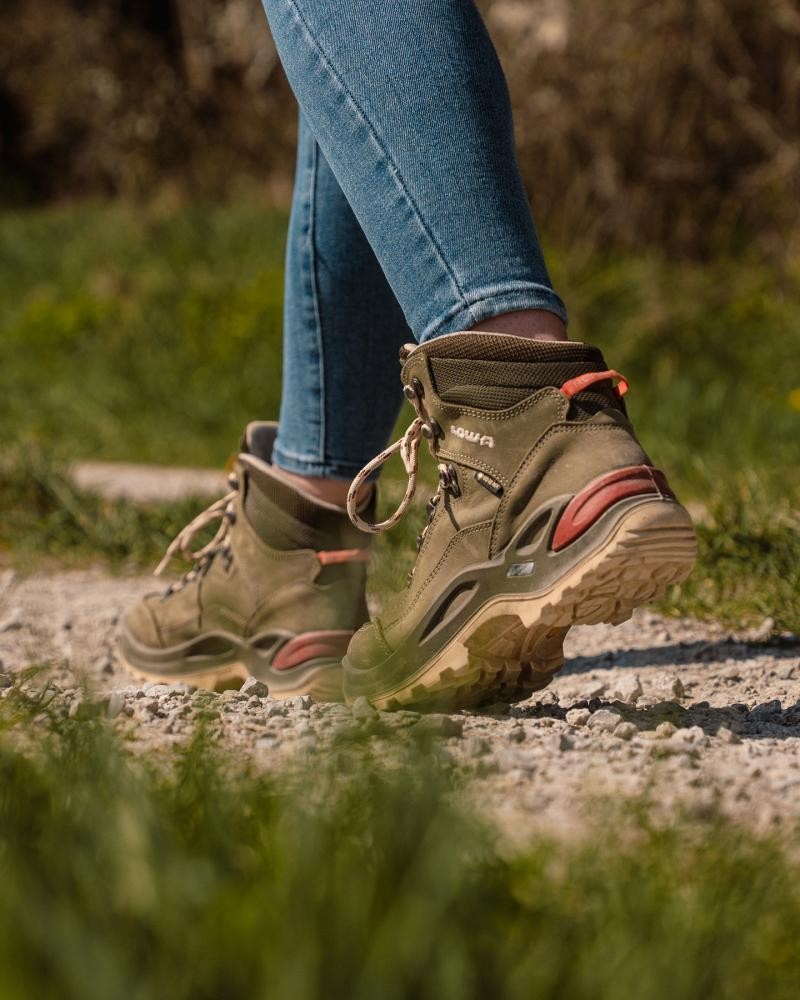 Es sind nur die Beine zu sehen, die Person wandert in Wanderschuhen auf einem geschotterten Weg