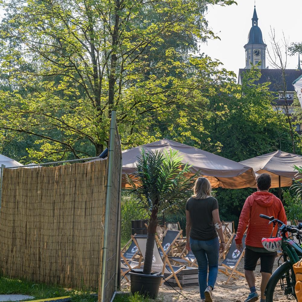 Zwei Personen laufen über den Stadtstrand, zu sehen sind Liegestühle 