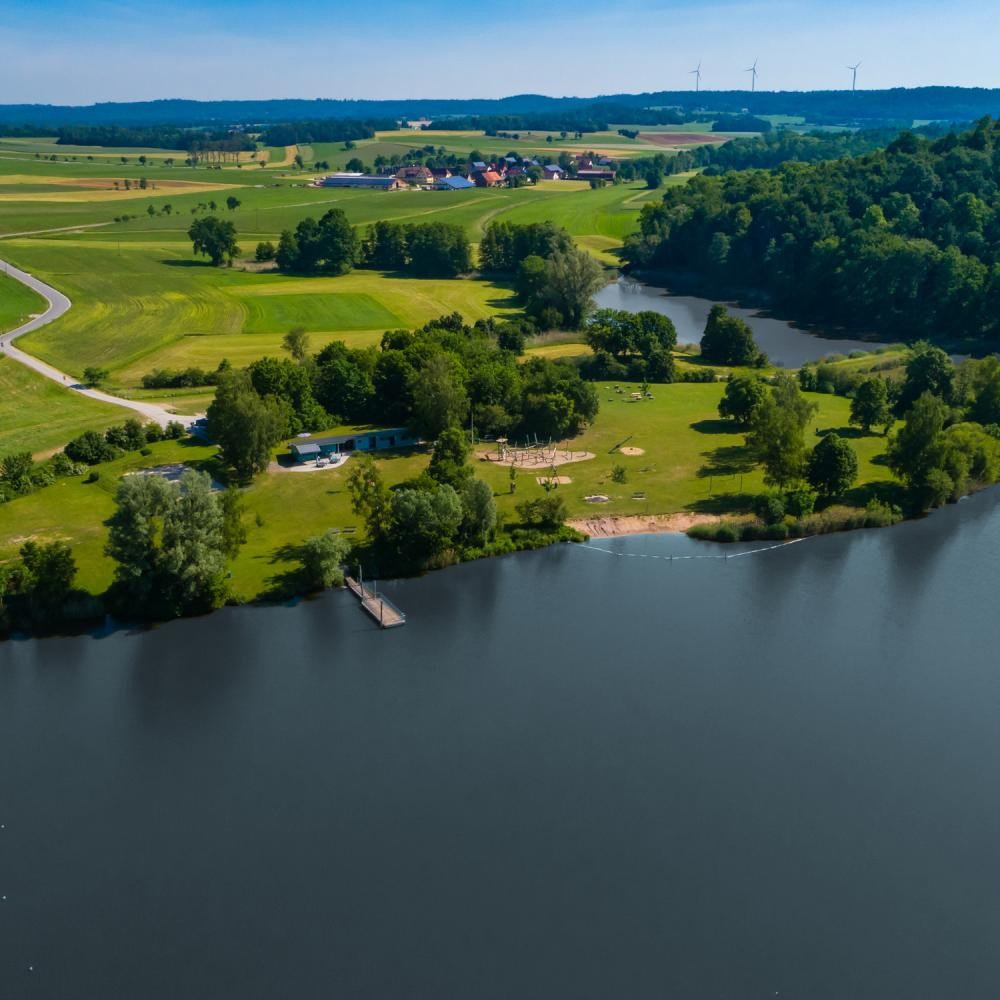 Blick auf den Degenbachsee mit Steg, Sandfläche, Volleyballfeld und Kiosk