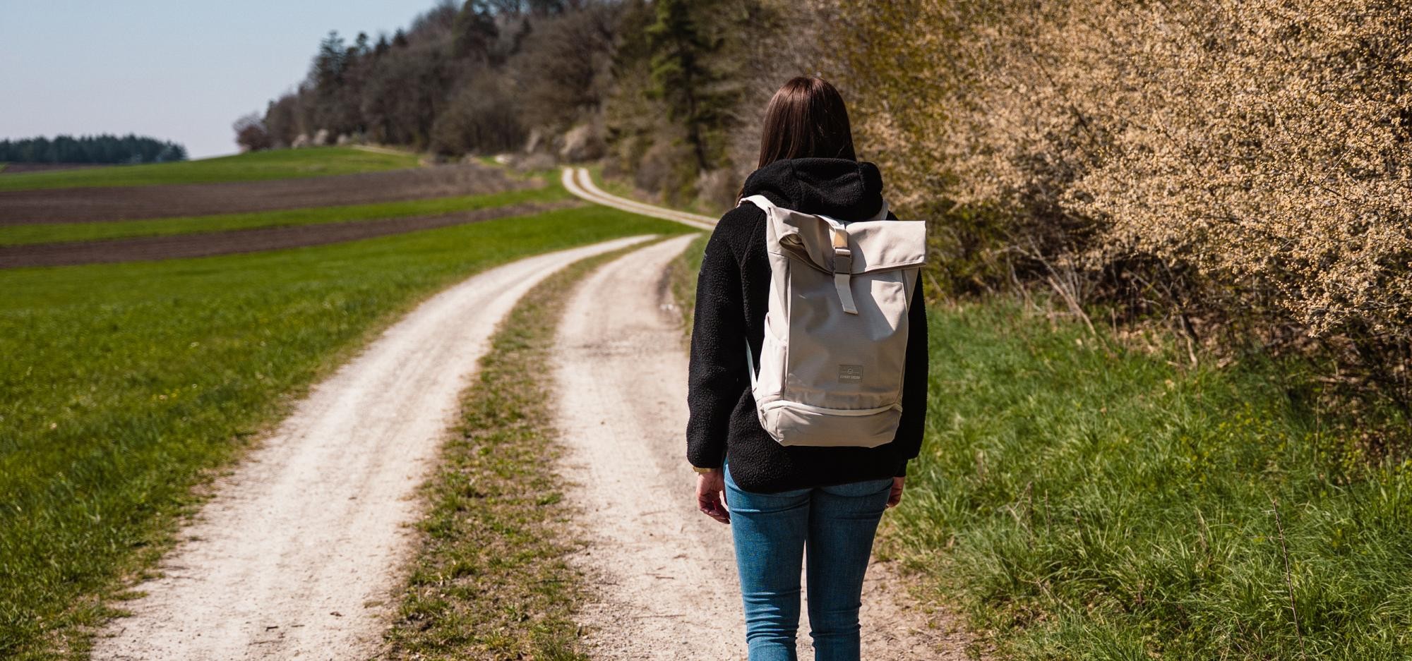 Frau mit Rucksack wandert auf geschottertem Weg am Waldrand